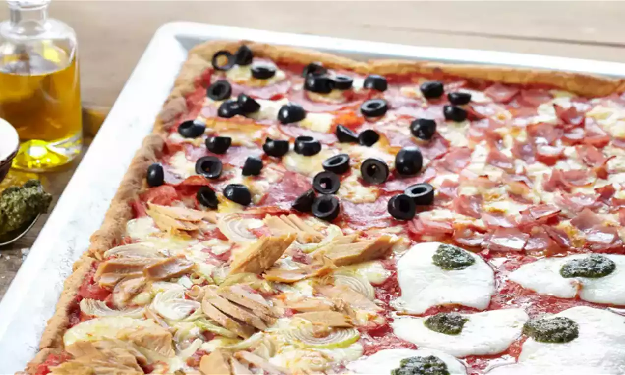 Pravokutna pizza tankog zlatno-smeđeg tijesta podijeljena na četvrtine s crnim maslinama, pršutom, artičokama i mozzarellom na crvenoj podlozi