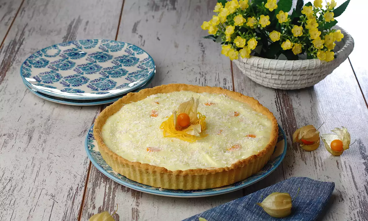 Altın rengi tart tabanı üzerine kremalı kazandibi dolgusu, ortasında altın çilek ve pudra şekeri, seramik tabaklar ve çiçeklerle sunulmuş