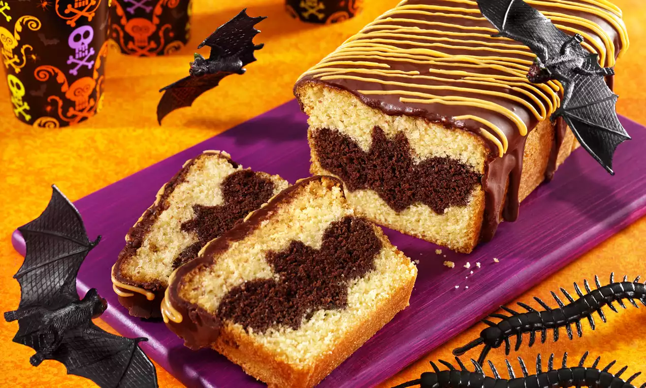Vaaleankeltainen kakkuleipä, jonka sisällä suklaaruskea lepakkokuvio, päällä suklaakuorrutetta ja keltaisia raitoja violetilla tarjoilualustalla