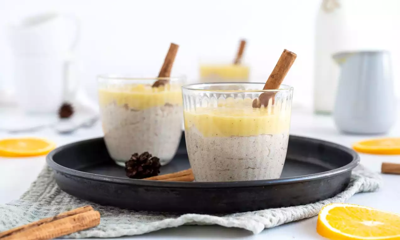 Glas mit beigem Grießbrei, gelber Orangen-Vanillesauce und dekorativer Zimtstange, serviert auf schwarzem Teller mit Orangenstücken