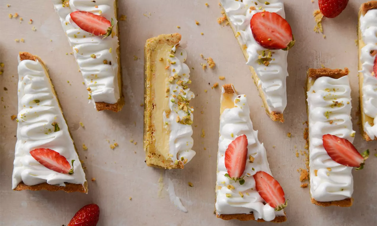 Пролетен тарт с хрупкав блат, слой крем с ванилено-жълт оттенък, пухкавата текстура на белия маскарпоне покрив с резени ягоди и поръски шамфъстък