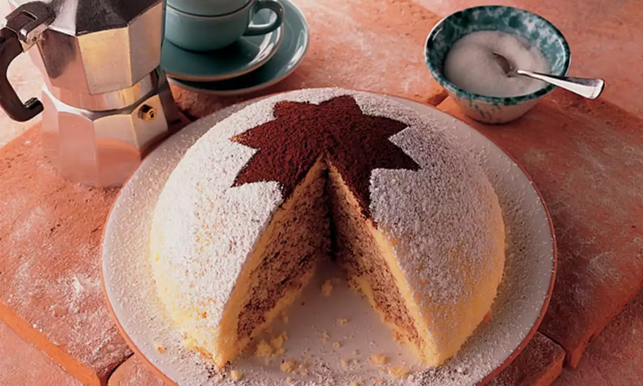 Yuvarlak şekilli, üzeri pudra şekeri kaplı, kakao ile yıldız deseni yapılmış ve içinde iki renkli dokusu görünen kek bir tabakta sunulmuş