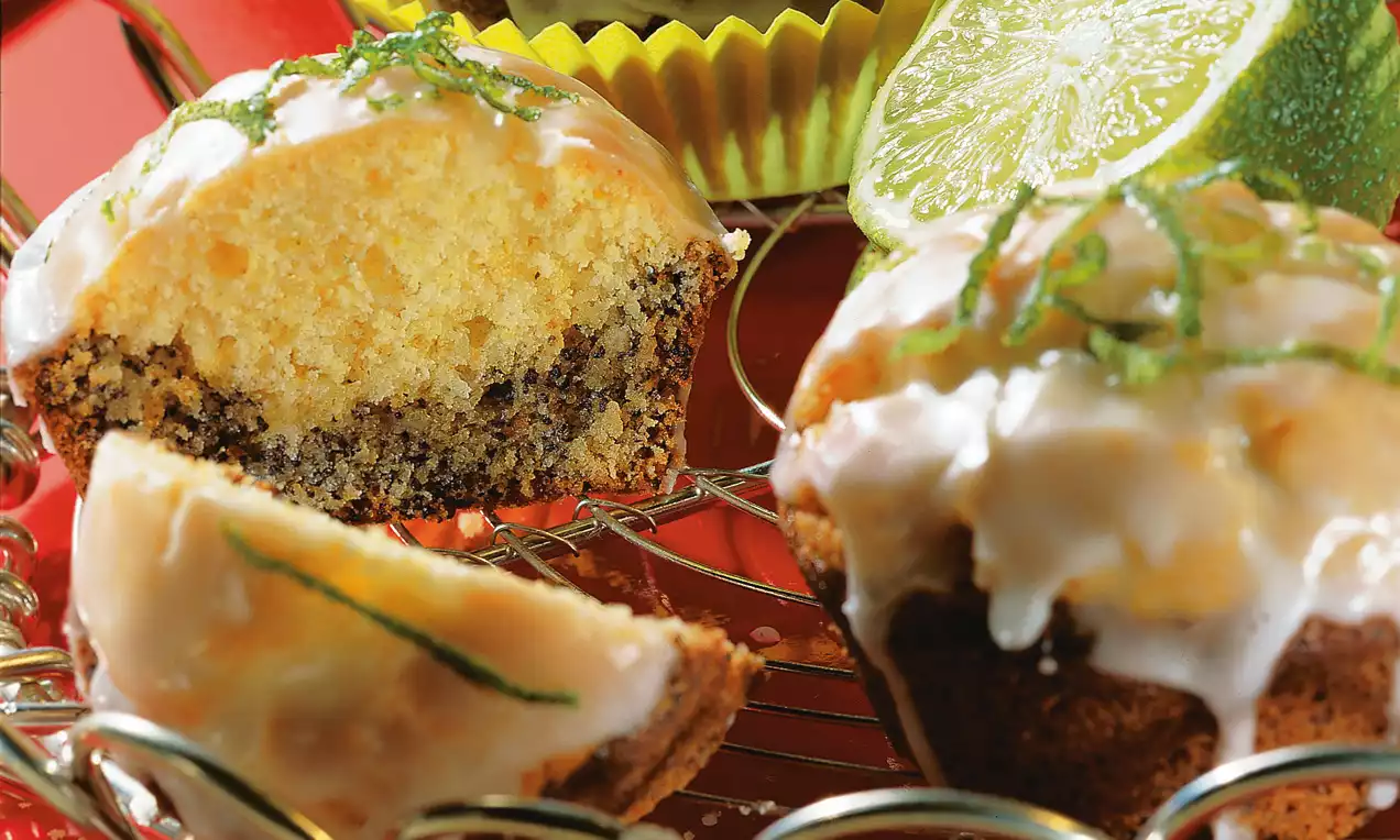 Muffins dorés moelleux au cœur parsemé de graines de pavot, glacés et garnis de zestes de citron vert sur une grille métallique