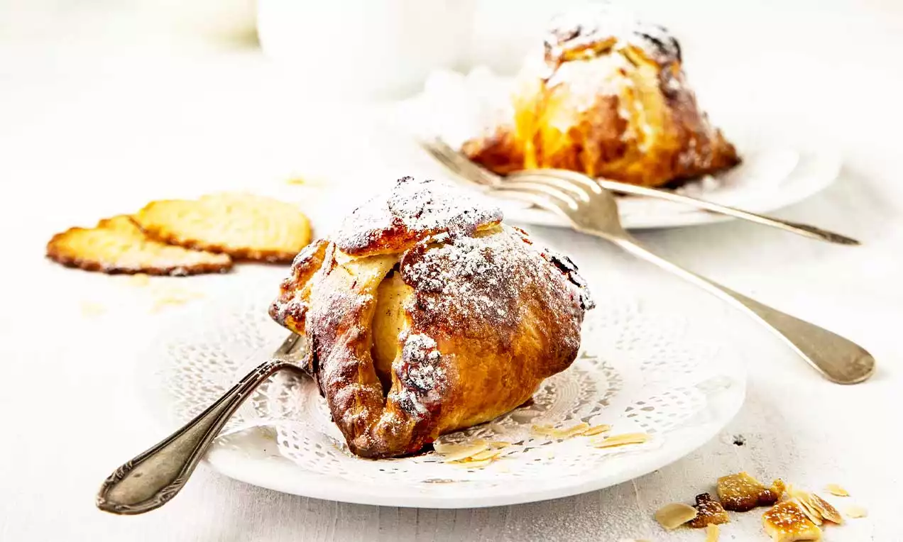 Pommes enrobées de pâte feuilletée dorée croustillante saupoudrées de sucre glace sur une assiette blanche avec une fourchette et quelques miettes
