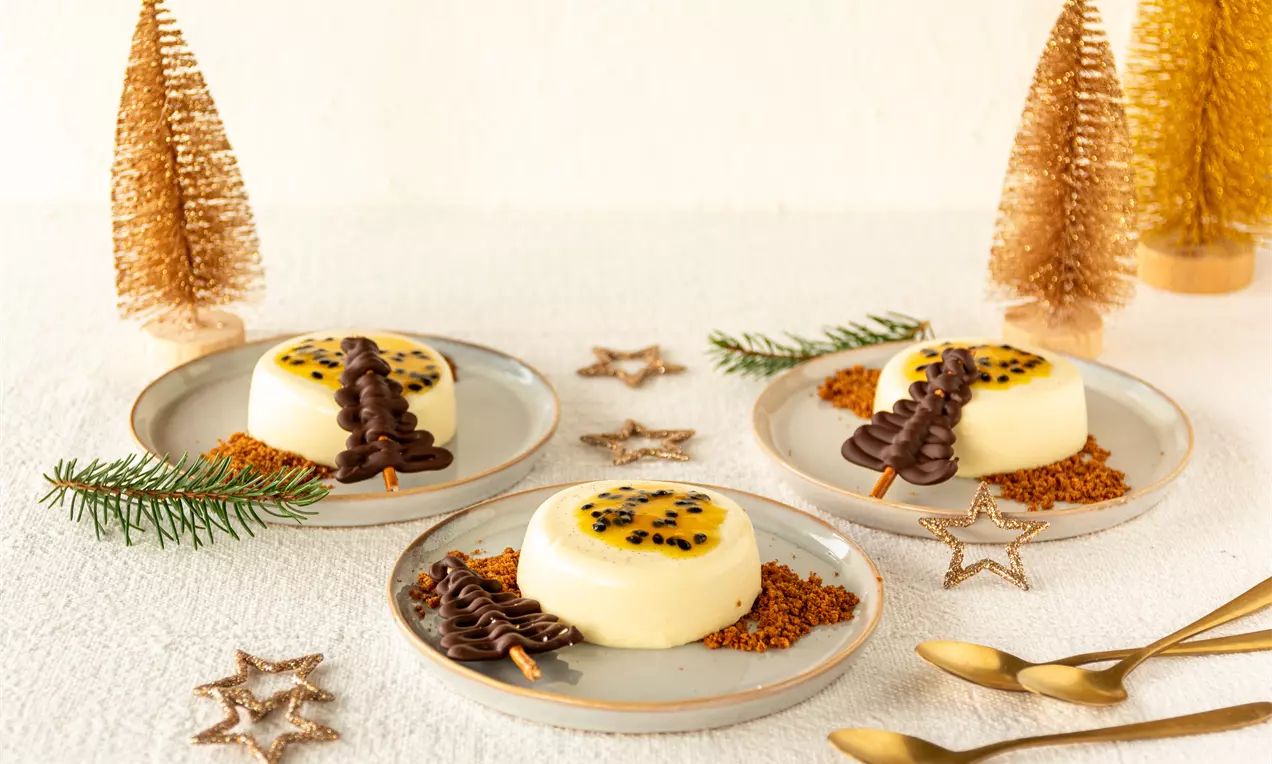 Panna cotta ivoire ornée de fruit de la passion et sapin chocolat sur lit de crumble caramel, entourée de déco dorée et couverts