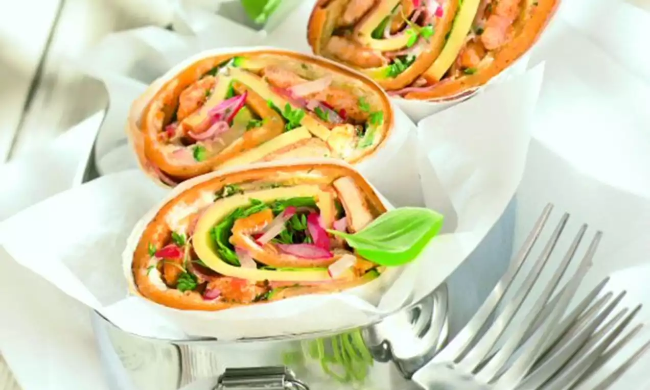 Mediterrane Wraps mit buntem Gemüse und zarter Füllung, spiralförmig geschnitten, in weißem Papier serviert auf einem silbernen Teller