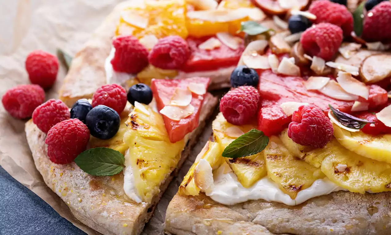 Pizza sucrée garnie de fruits frais colorés comme framboises, myrtilles, ananas grillé, fraises et copeaux de noix de coco sur une base moelleuse
