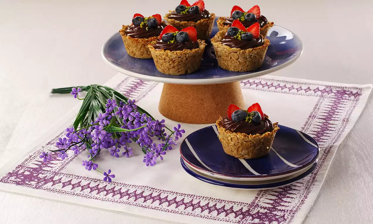 Tatlı sepetler gevrek kahverengi tabanlı, üzerine çikolata kreması, canlı kırmızı çilek ve parlak mavi yaban mersinleriyle süslenmiş