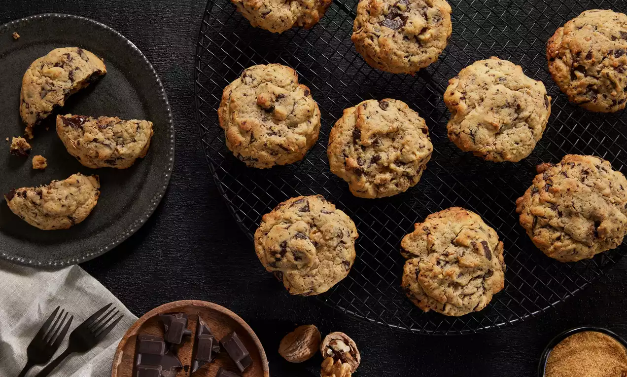 Büyük taneli çikolata parçacıklı, yuvarlak ve iri New York kurabiyeleri, tel ızgara üzerinde sıralı, yanında ceviz ve şekerle sunulmuş