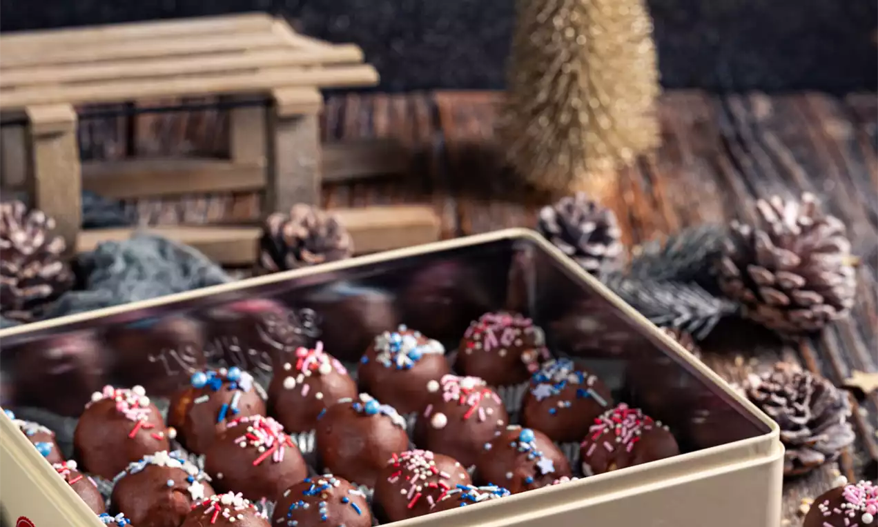 Čokoladne kroglice sijoče temnorjave barve, posipane z barvnimi mrvicami, natančno zložene v kovinsko škatlo in nekaj na krožniku z zvezdico