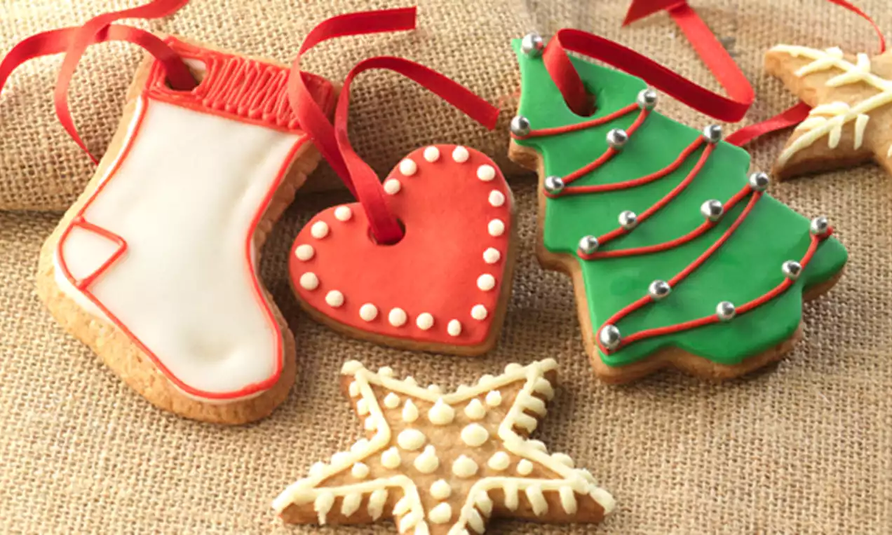 Galletas navideñas decoradas con glaseado blanco, rojo y verde, formas de árbol, corazón y estrella, sobre tela de arpillera