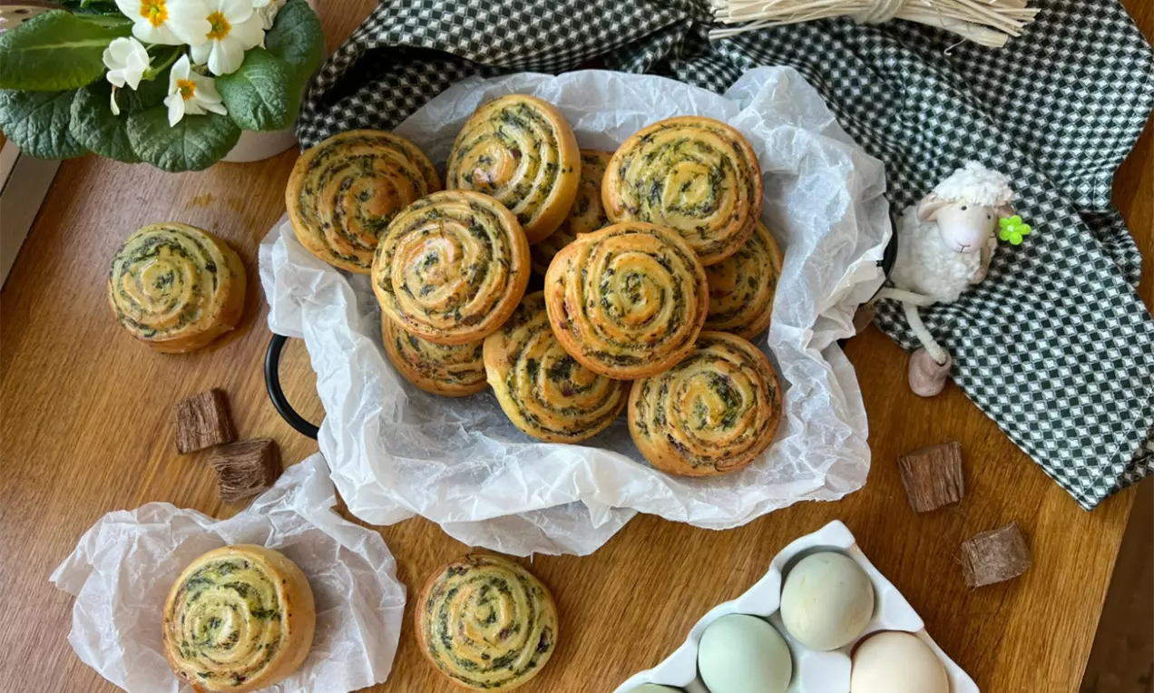 Slimáky zlatohnedej farby s pravidelnou špirálovou textúrou a zelenou špenátovou plnkou, uložené na papieri v košíku na drevenom stolíku