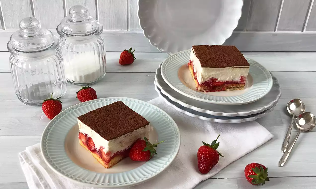 Tiramisu mit weißer Schicht und Kakaopulver, Erdbeeren und hellgelben Biskuit auf weißen Tellern mit frischen Erdbeeren dekoriert