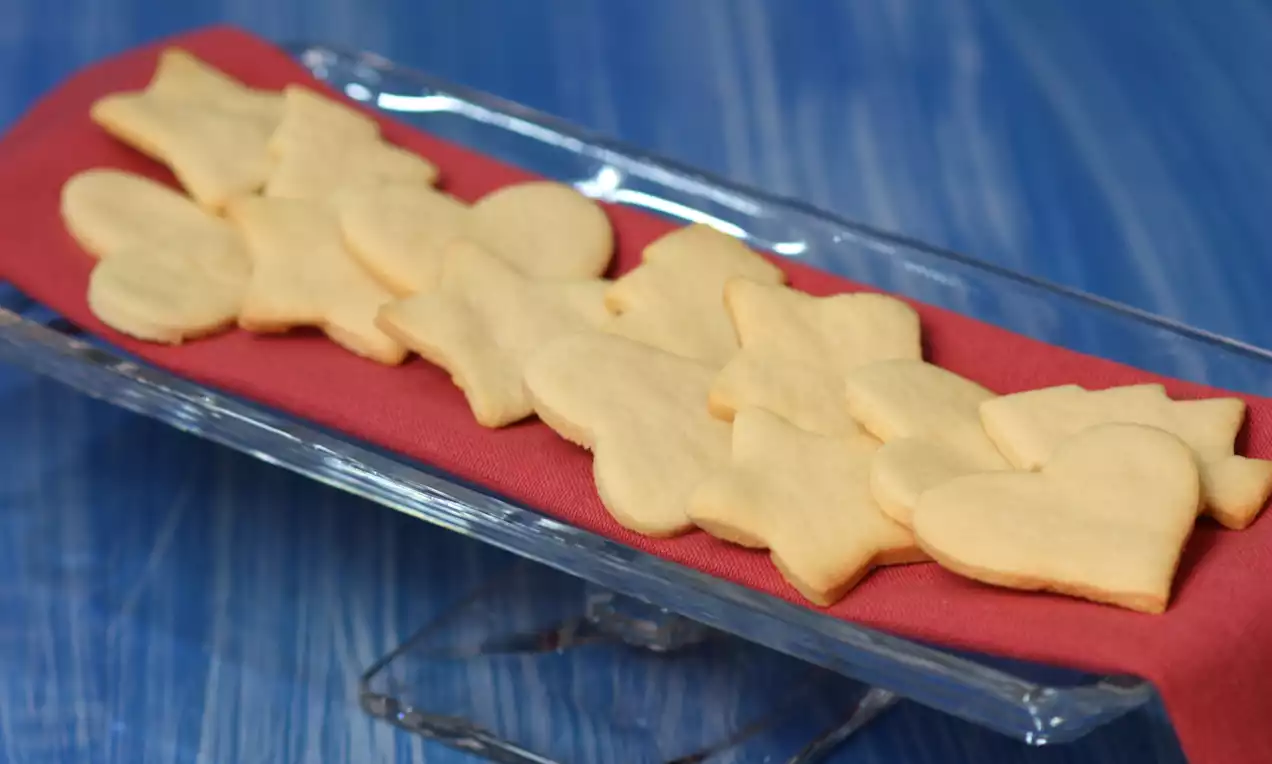 Cam bir tabakta kırmızı bir bez üzerinde kalp, yıldız ve çiçek şekilli açık sarı renkli sade bisküviler 