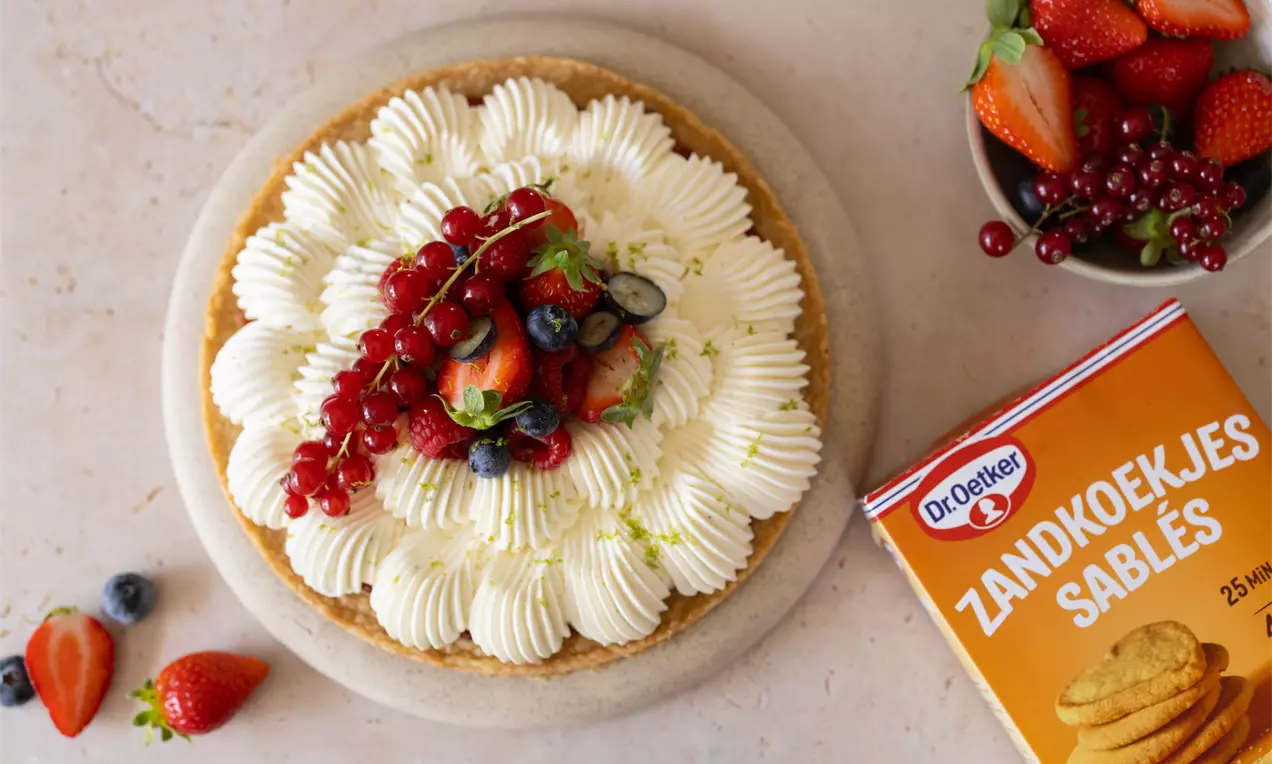 Tarte aux fruits avec une base sablée dorée, crème vanillée en rosettes et garniture de baies rouges, fraises et myrtilles sur une assiette
