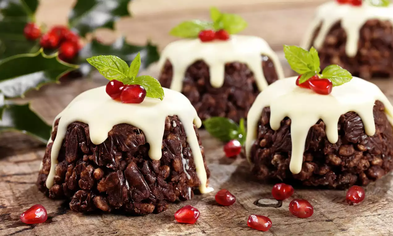 Crispy chocolate puddings with a glossy white glaze, topped with red pomegranate seeds and green mint leaves on a rustic wooden surface