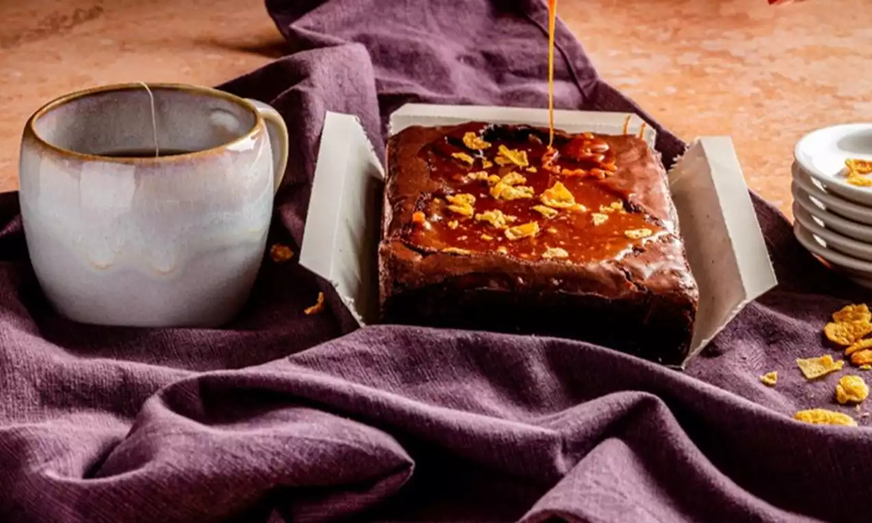 Brownies moelleux couleur cacao avec une surface lisse et brillante, garnis de cornflakes dorés et entourés de tissu violet