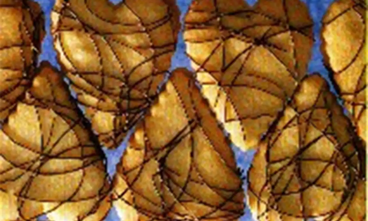Petits sablés dorés en forme de cœur, décorés de fines lignes de chocolat noir sur un fond bleu