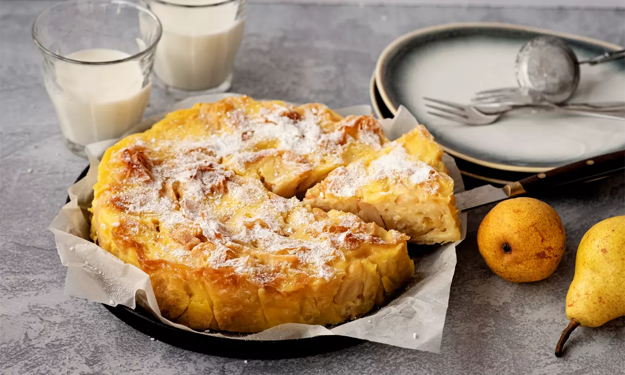 Галактобуреко със златиста, леко ронлива коричка и сочна плънка с парченца круши, поръсено с пудра захар върху пергамент в черна тава