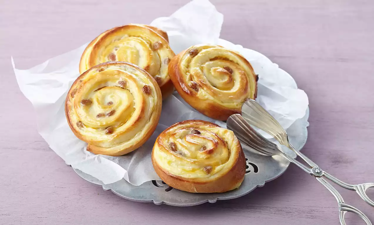 Goldbraune Puddingschnecken mit cremiger Füllung und Rosinen, auf weißem Pergamentpapier auf einer silbernen Platte angerichtet