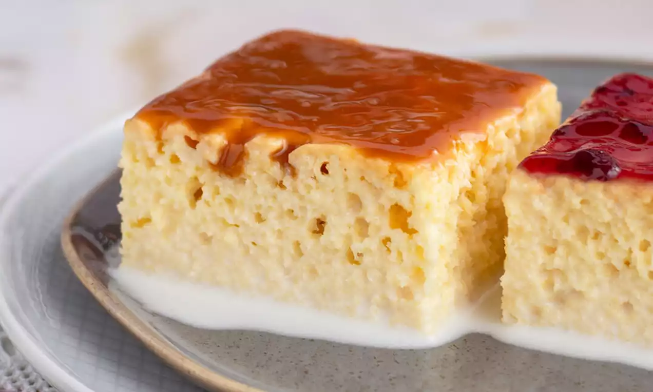 Dvije kocke trileće, svijetložute boje s rupičastom teksturom, prelivene tankim slojem karamele i crvenog voćnog preljeva, na sivom tanjiru