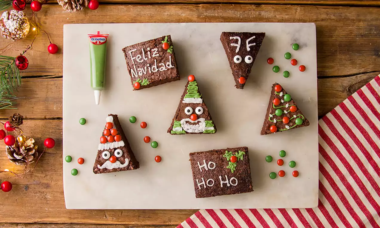 Brownies triangulares de chocolate oscuro decorados con glaseado blanco, ojos de azúcar, letras y grageas coloridas en una tabla