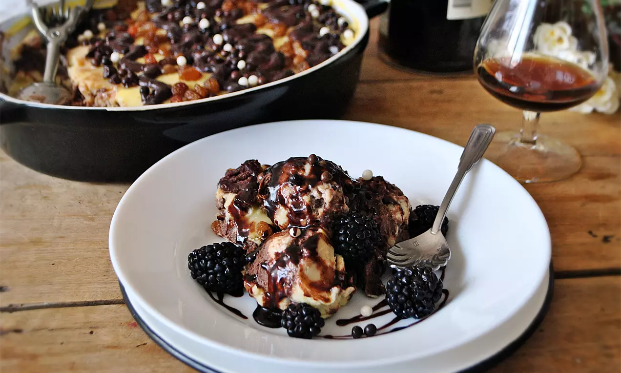 Бисквитена торта с кремообразни пластове и тъмен шоколад, поднесена на чиния с къпини и шоколадов сос