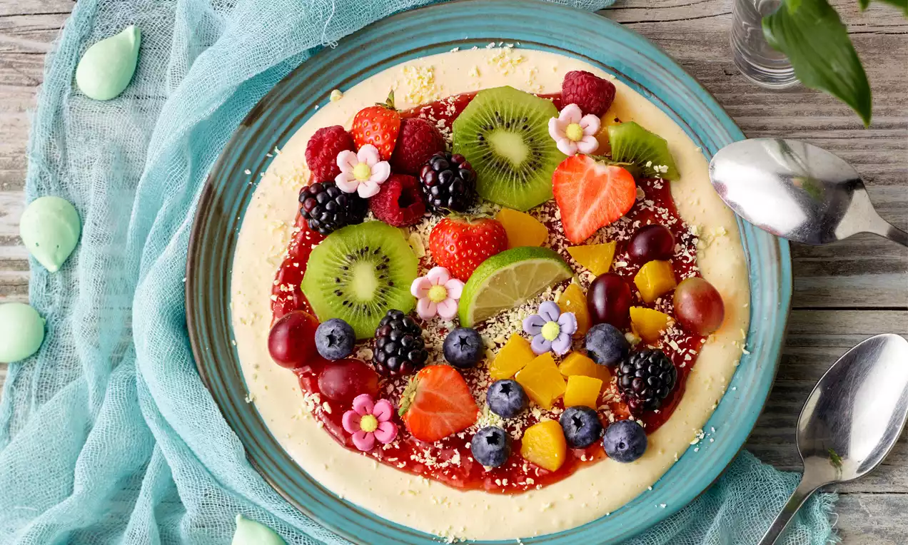 Bunte Eis-Pizza aus cremigem Vanilleboden mit roter Fruchtsauce, frischen Beeren, Kiwi-Scheiben, Mangostückchen und essbaren Blüten