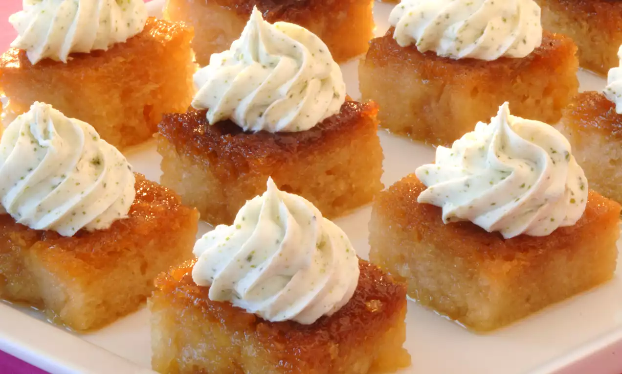 Altın renginde nemli ekmek kadayıfı dilimleri üzerinde beyaz krema rozetleri, pürüzsüz ve hafif dokulu görünüyor