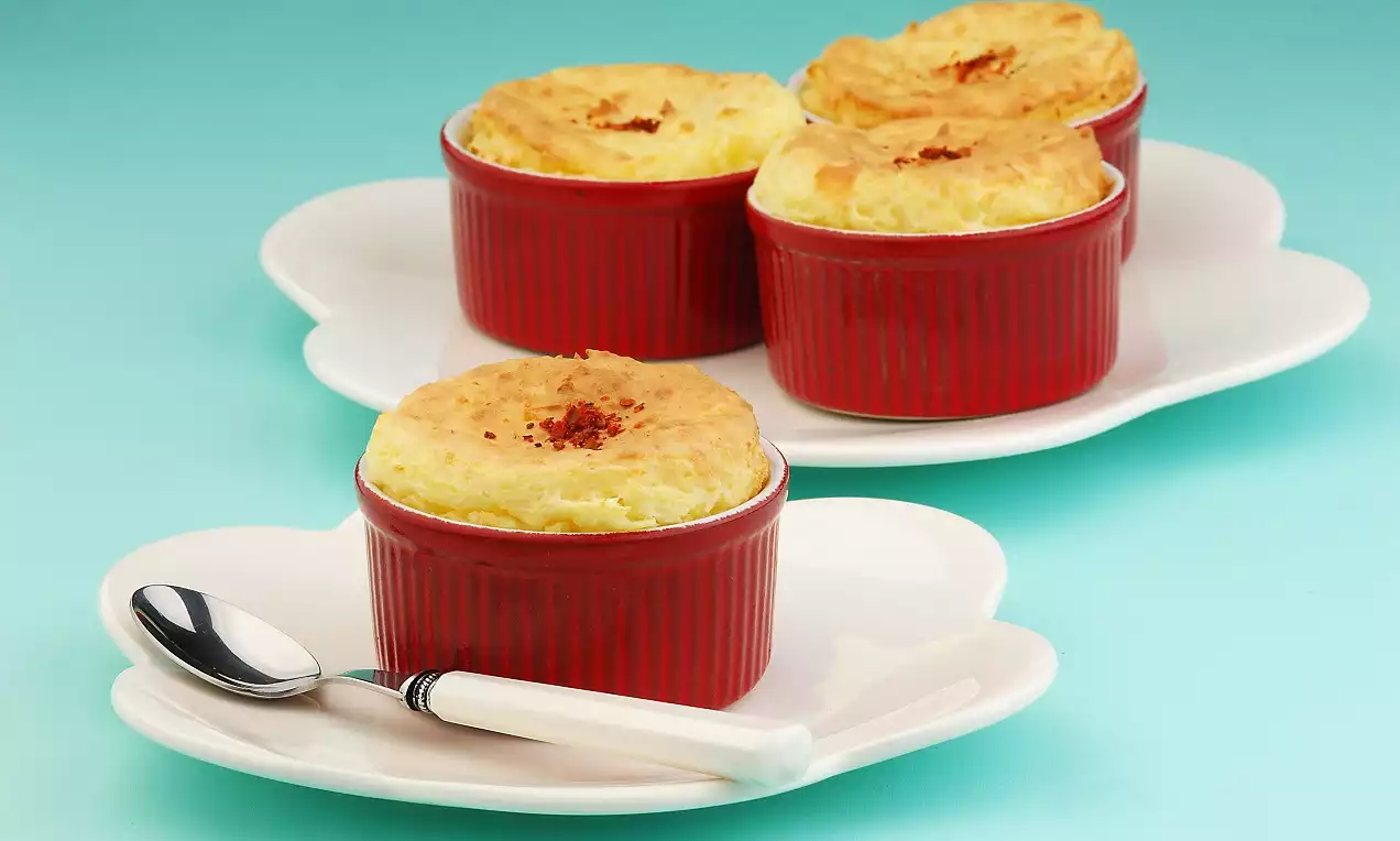 Kırmızı seramik kaplardaki altın sarısı kabarık patatesli ve peynirli sufleler beyaz kalp şeklindeki tabakta gümüş uçlu bir kaşıkla sunulmuş