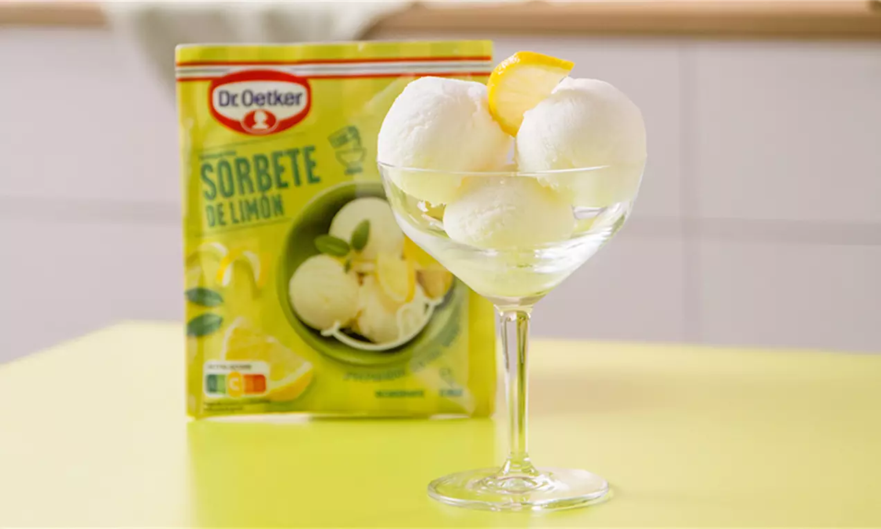Bolas de sorbete blanco con textura aterciopelada en copa de cristal adornada con rodaja de limón amarillo sobre mesa amarilla