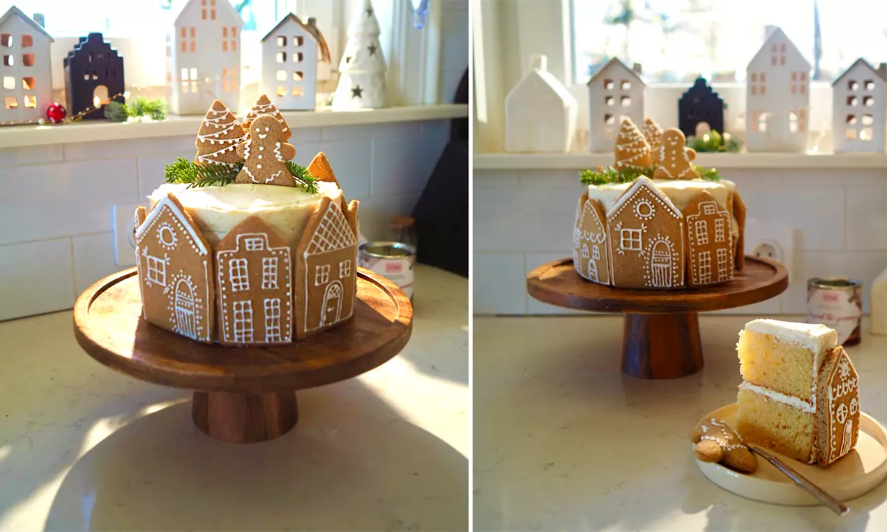 Портокаловата торта с меденки е декорирана с къщички от медено тесто и поръсена с бяла глазура, поставена върху дървена стойка