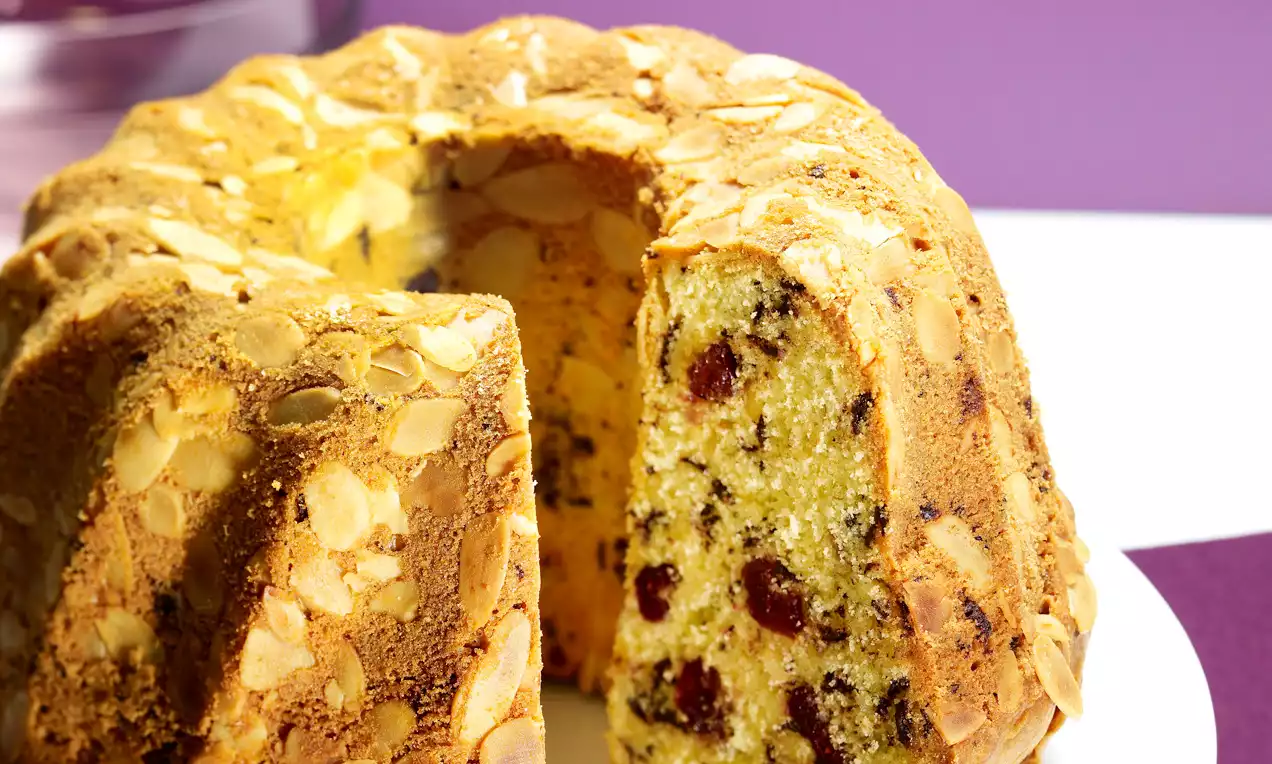Gâteau Bundt moelleux doré, incrusté d'amandes effilées croquantes, avec intérieur jaune parsemé de canneberges et pépites de chocolat