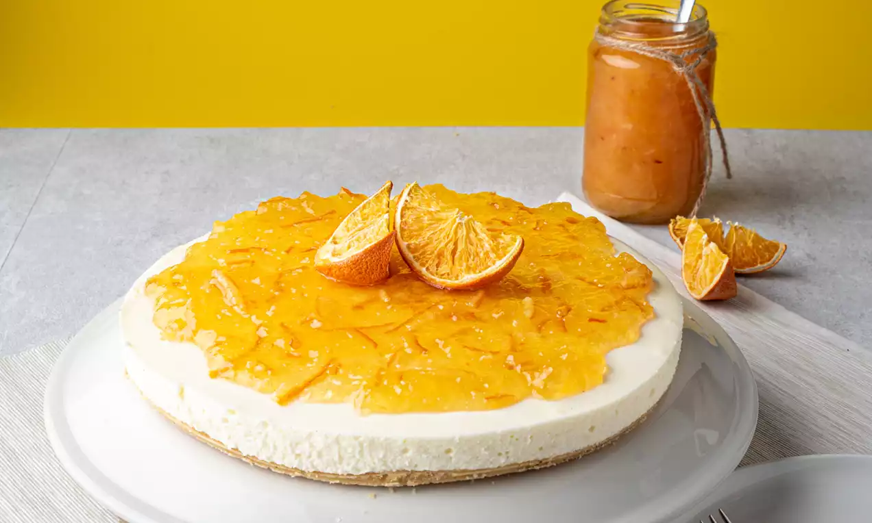 MonChoutaart met een gladde vanillecrème op een koekbodem, bedekt met glanzend sinaasappeltopping en schijfjes sinaasappel op een wit bord
