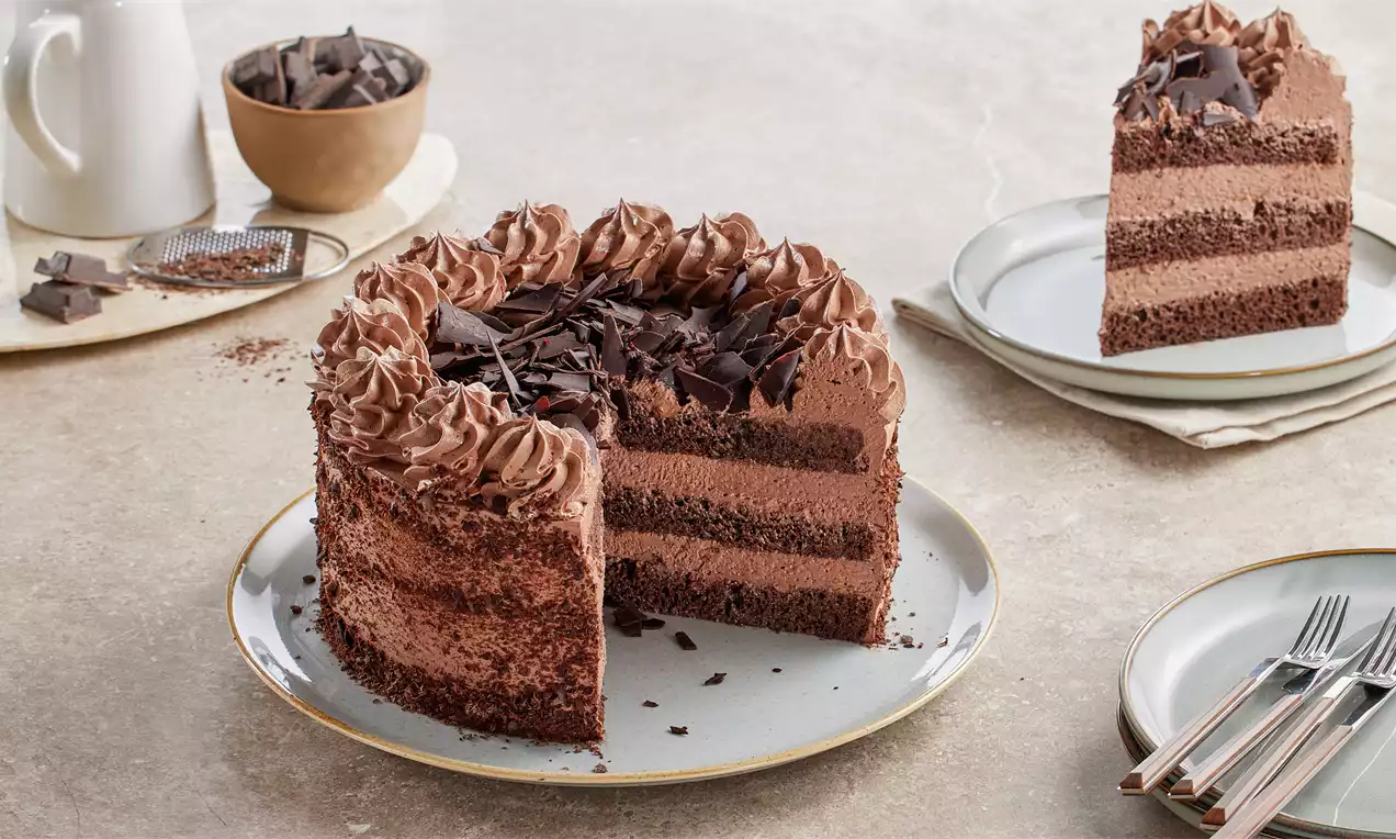 Kakao kaplı beyaz tabakta, kıvrımlı krema ile süslenmiş, kat kat çikolatalı kek parçalarıyla dekore edilmiş çikolatalı pasta