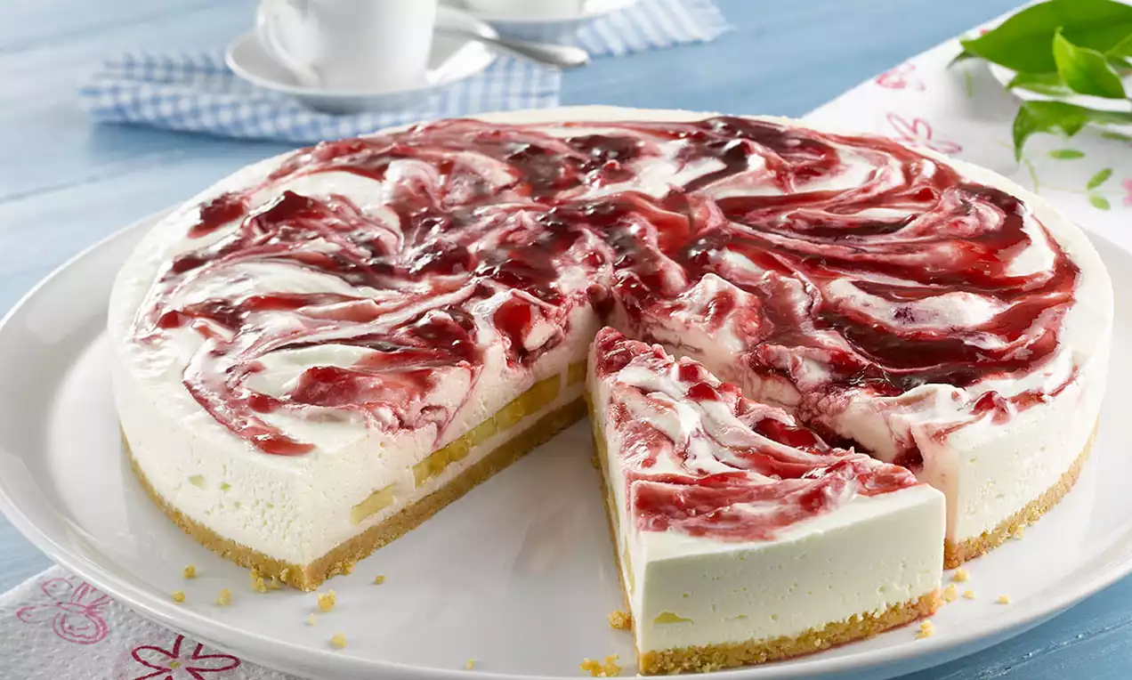 Okrugla torta sa svijetlom kremom i slojem višanja u crveno-bijelim kovitlacima, na biskvitnoj podlozi, poslužena na bijelom tanjiru