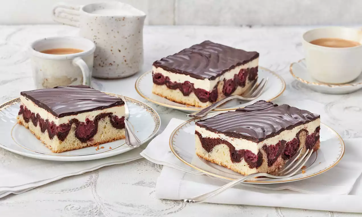 Donauwellen mit hell-dunklem Biskuit, saftigen roten Kirschen, zarter Vanillecreme und glänzender Schokoladenglasur, auf Teller serviert