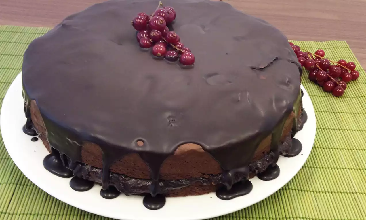 Ronde chocoladetaart met glanzende donkerbruine ganache, druipend langs de zijkanten, gegarneerd met een tros rode aalbessen op een wit bord