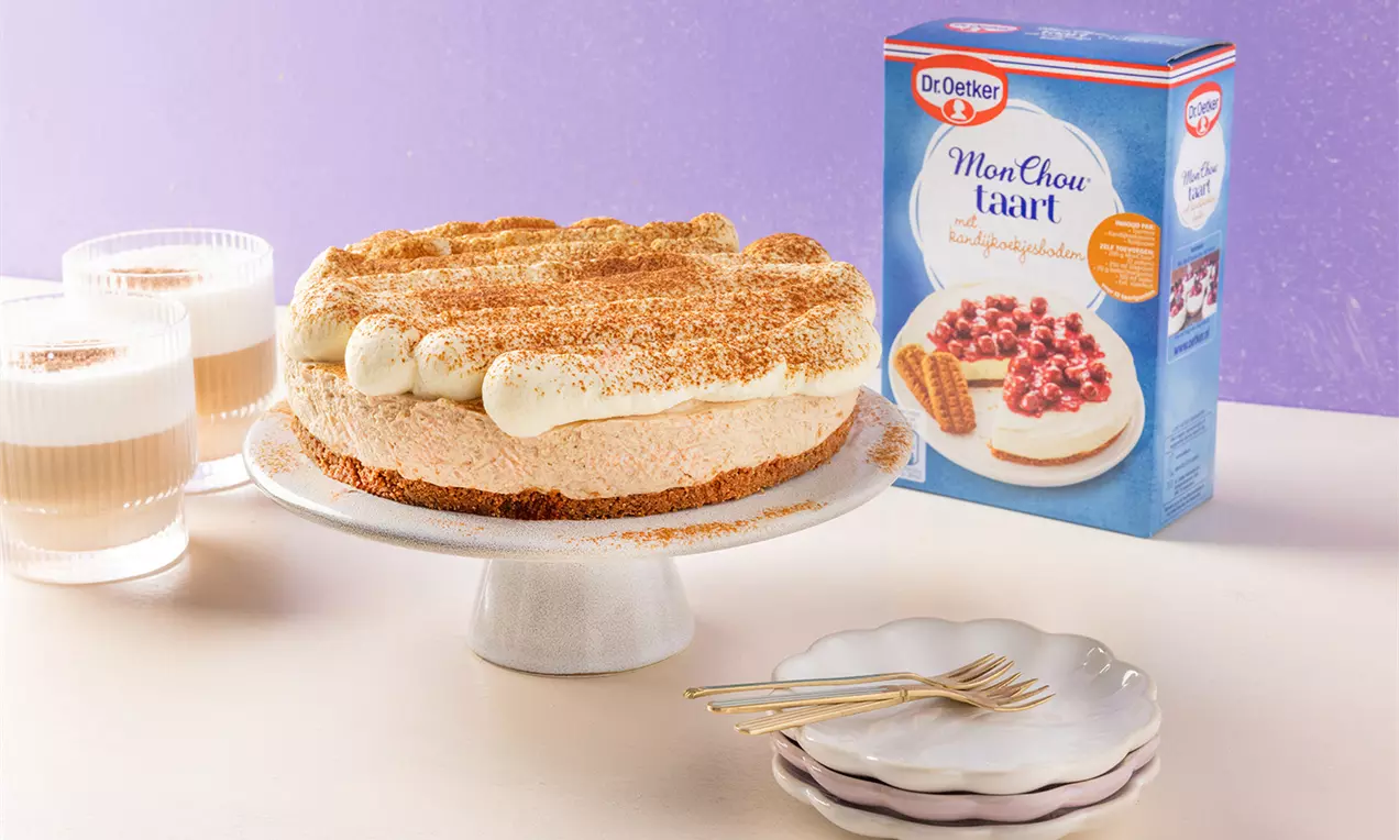 Romige Chai cheesecake met kruidige laag op een witte voettaartschaal, gedecoreerd met kaneel en slagroomtoefjes, tegen een paarse achtergrond