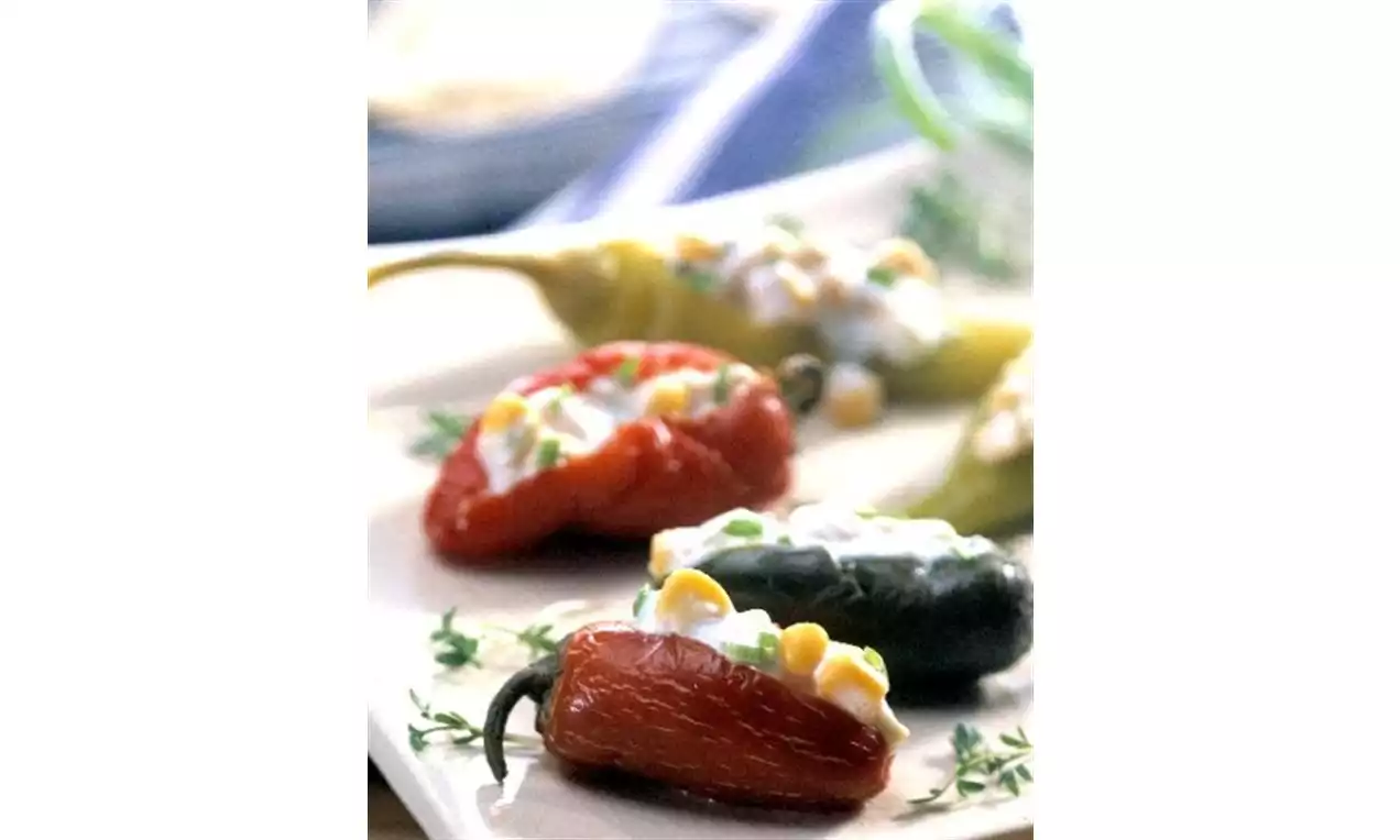 Bright stuffed peppers in shades of red, green and yellow topped with creamy filling, corn kernels and herbs on a white plate
