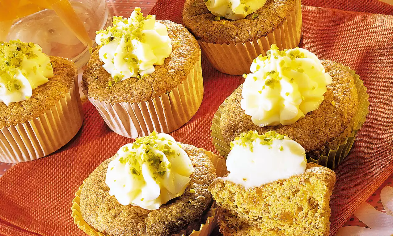 Kleine Rübli-Törtchen mit goldbrauner Kruste, weißer Sahnehaube und gehackten Pistazien auf rotem Stoff angerichtet