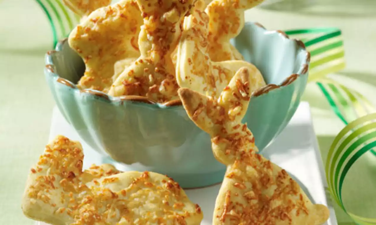 Goudgele kaashaasjes met geraspte kaas bovenop, knapperig gebakken en deels staand in een lichtblauw schaaltje op een tafel