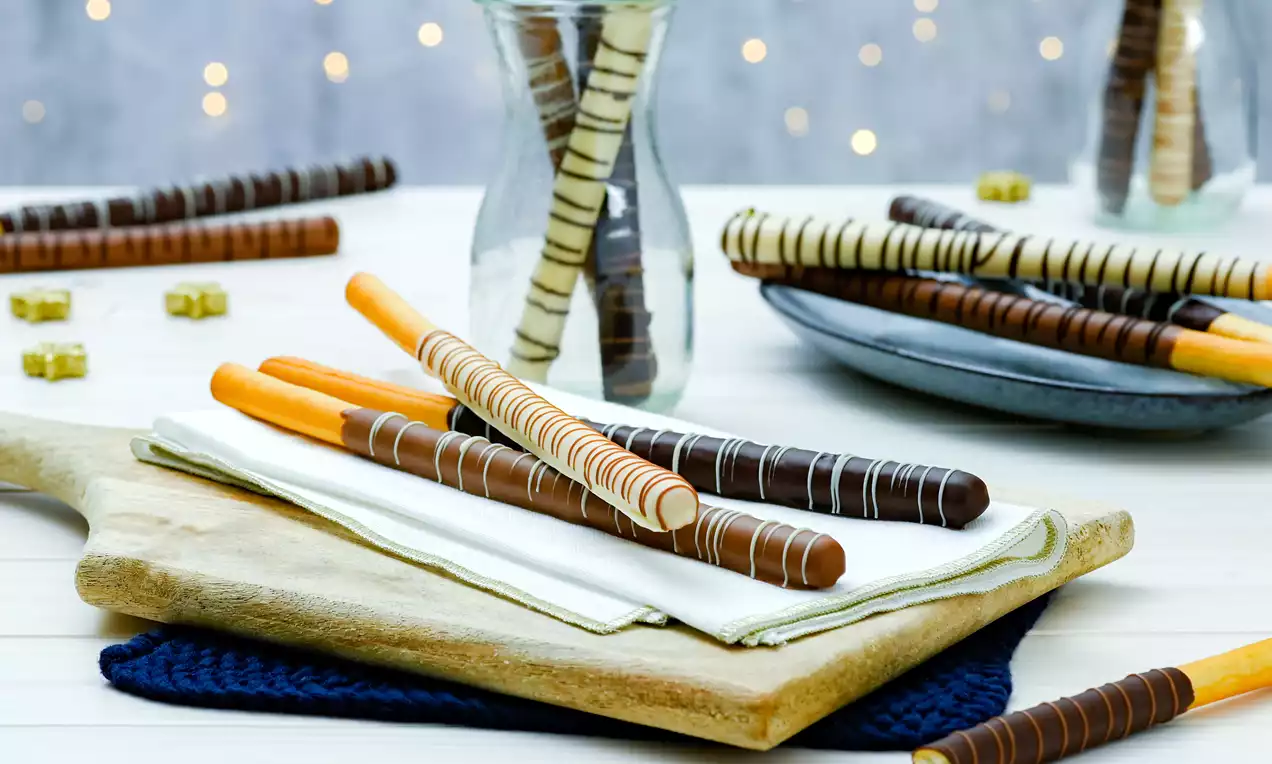 Čokoladni štapići glatke teksture s tankim prugama, uredno posloženi na drvenoj dasci preko bijelog platnenog ubrusa