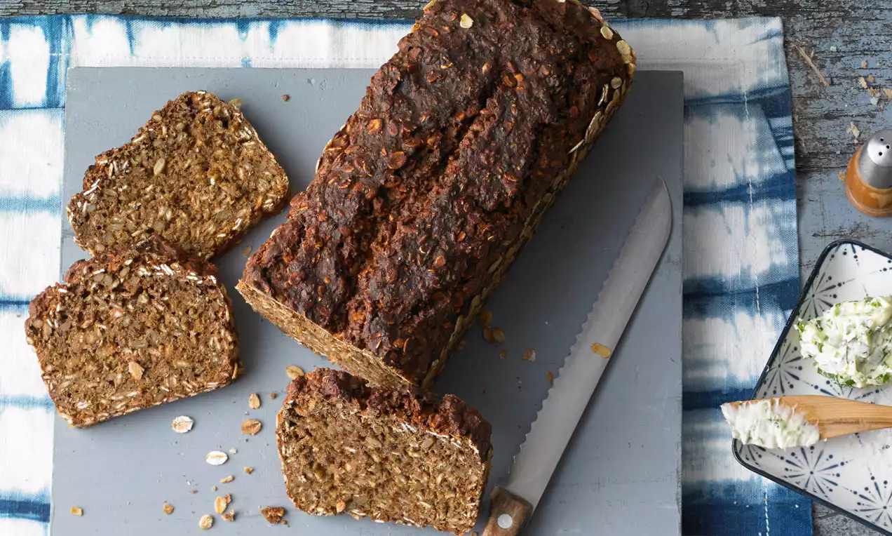 Dunkelbraunes, krustiges Schwarzbrot mit grober Textur, teils in dicke Scheiben geschnitten, angerichtet auf einem grauen Schneidebrett