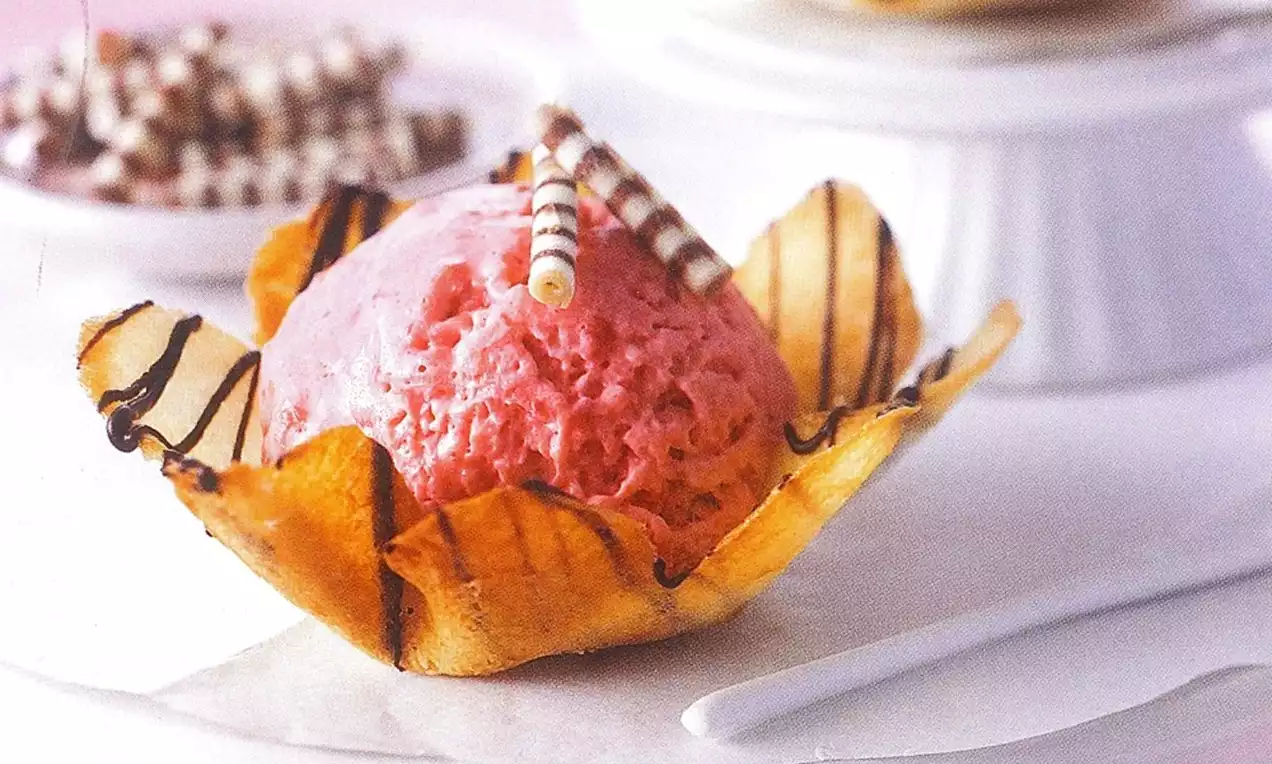 Boule de glace framboise rose vif dans une coupelle en biscuit doré rayé de chocolat, décorée de fins bâtonnets chocolatés