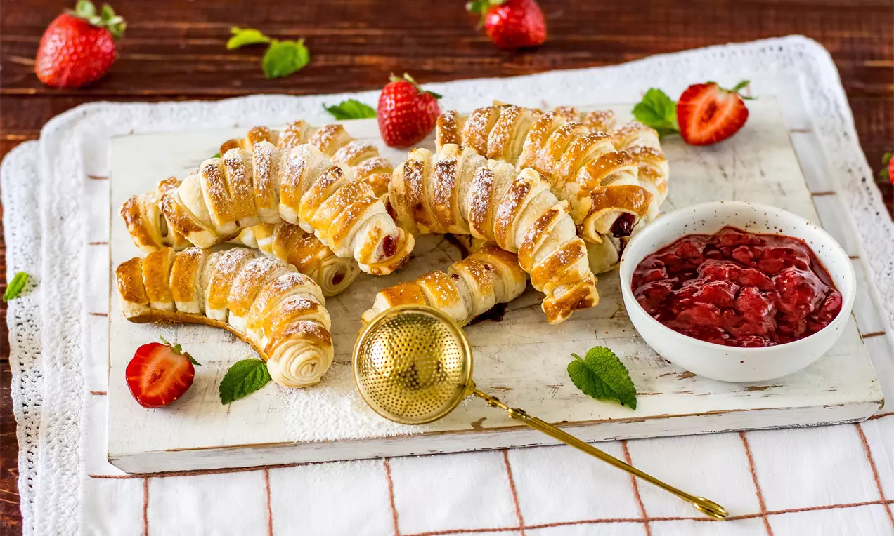 Златисти бутер кифлички с леко напукана текстура, пълни с ягодово сладко, подредени върху бяла дървена дъска, с пресни ягоди и купичка сладко