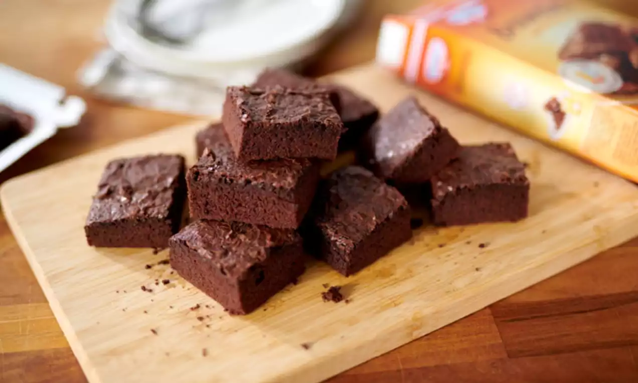 Carrés de brownies brun foncé à la texture dense et légèrement craquelée, empilés sur une planche en bois clair