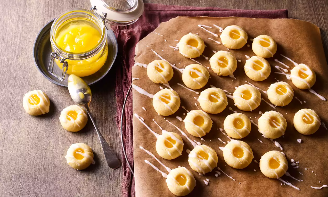 Puha, aranysárga omlós sütemények citromos krémmel töltve, egyenletesen sorba rendezve barna sütőpapíron fehér cukormázzal csíkozva