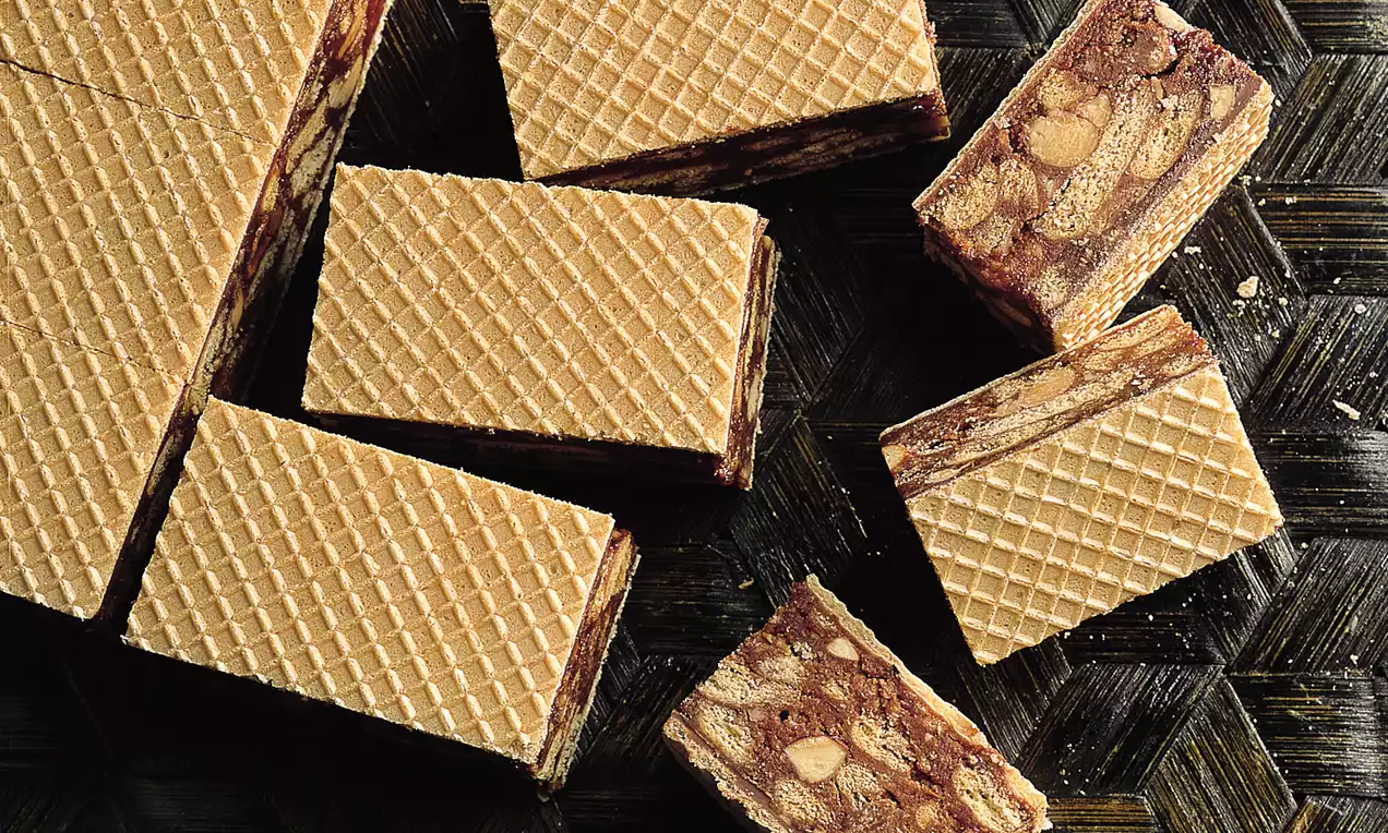 Knabberschnitten mit beigem Waffelmuster, rechteckig, gefüllt mit dunkler Schokoladen-Nuss-Masse auf dunklem, geflochtenem Untergrund