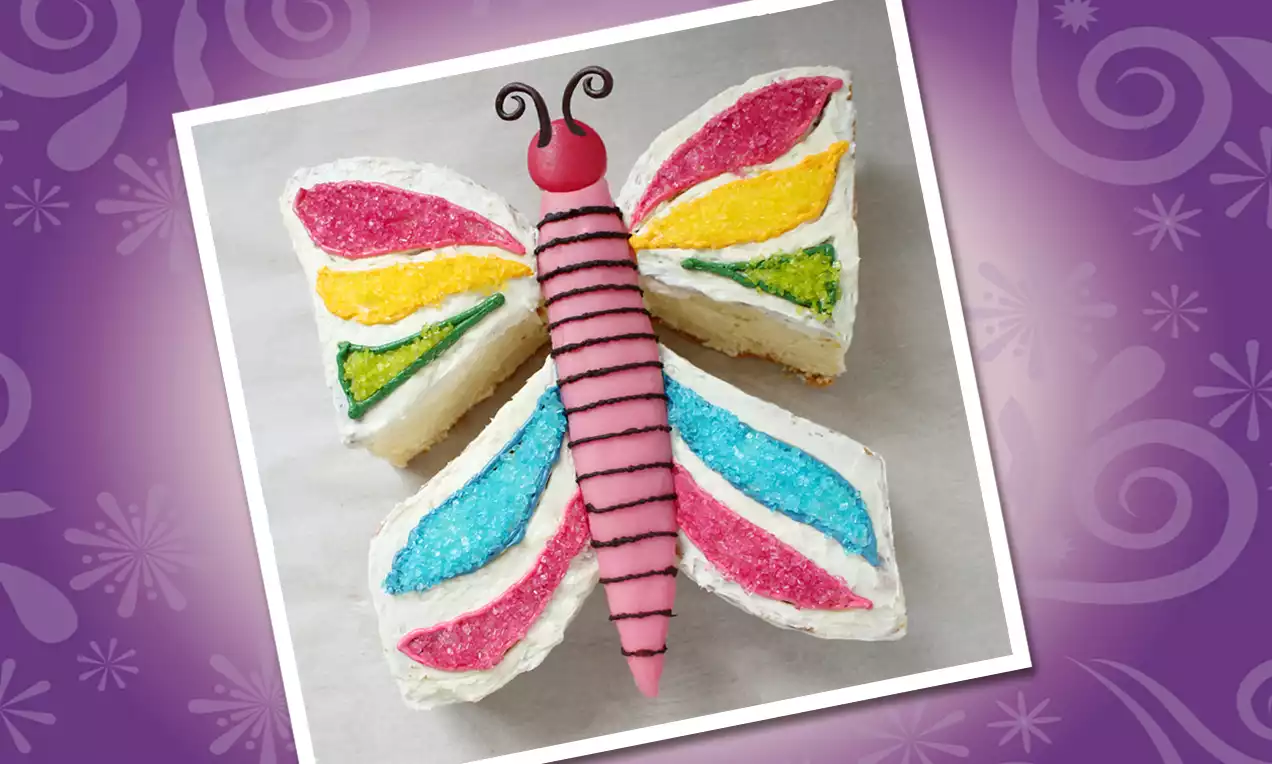 Vlindervormige taart met witte crème, felgekleurde vleugels, roze marsepeinen lijf en chocoladelijnen op een licht ondergrond